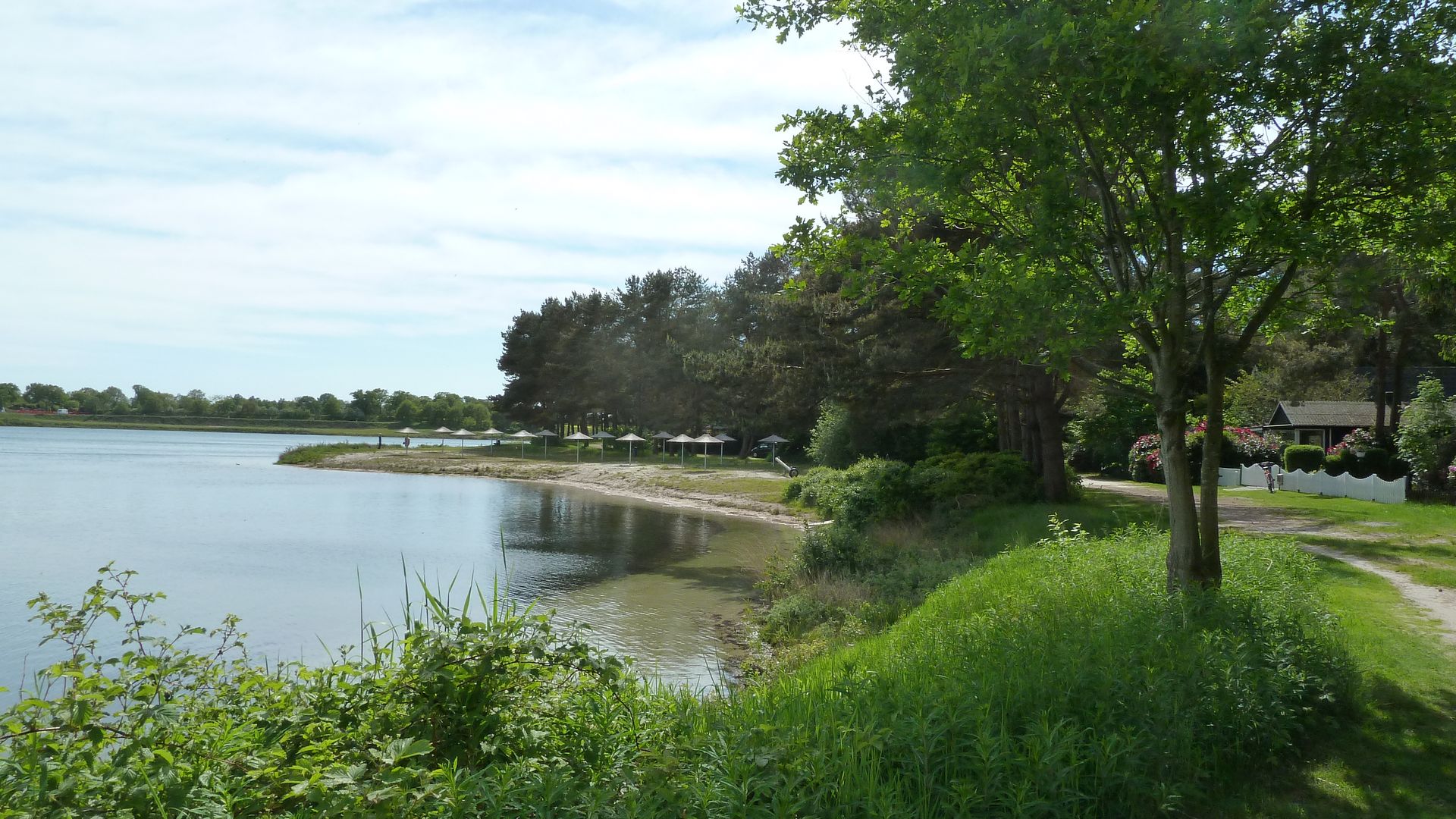 Blick vom Ufer auf den Sandstand mit Sonnenschirmen