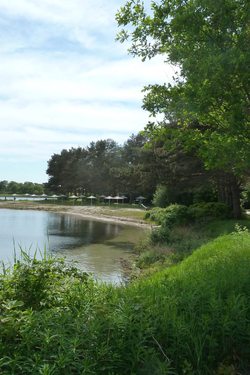 Blick vom Ufer auf den Sandstand mit Sonnenschirmen