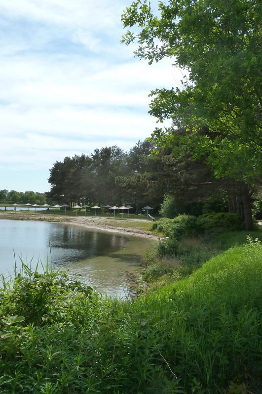 Blick vom Ufer auf den Sandstand mit Sonnenschirmen