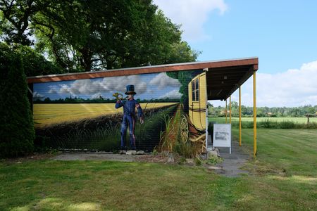 Außenansicht des Postmuseum Bokel. Die Wand ist handbemalt und zeigt einen uniformierten Mann mit Posthorn neben einer gelben Postkutsche vor einem Rapsfeld