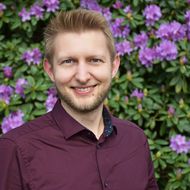 Mitarbeiter der Tourist-Information Wiefelstede vor einem lila blühenden Rhododendron