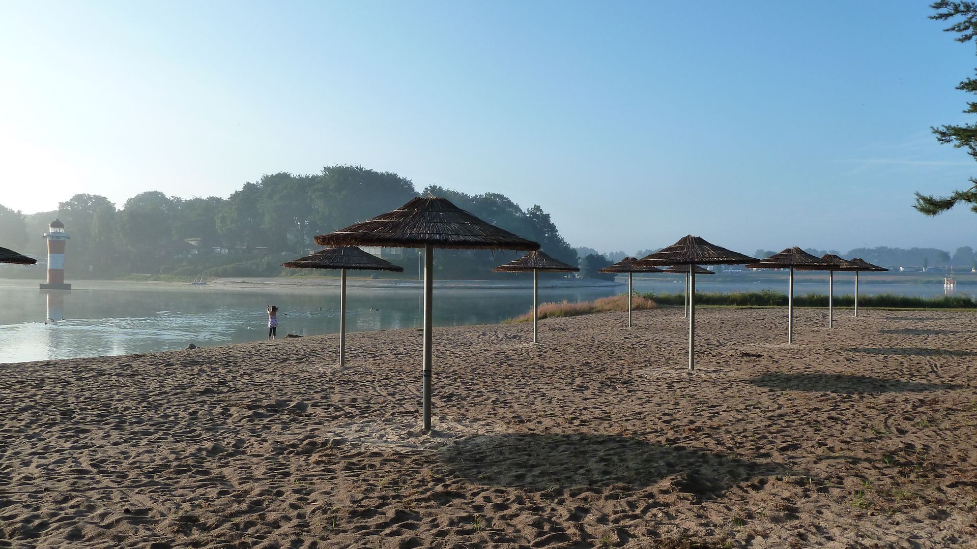 Sandstrand und Sonnenschirme in der Morgensonne am Bernsteinsee