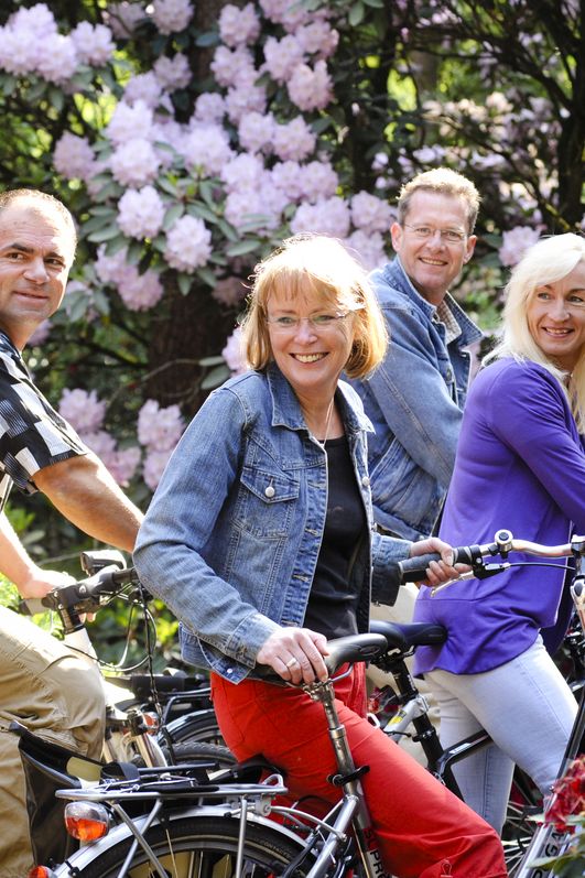 Eine Gruppe Radfahrer posiert vor bunten Rhododendren